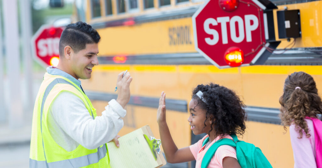 Image: Students are safely walking off their school bus accompanied by a crossing guard.